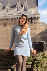 a lady in a black top, a blue tweed jacket and a blue tweed skirt